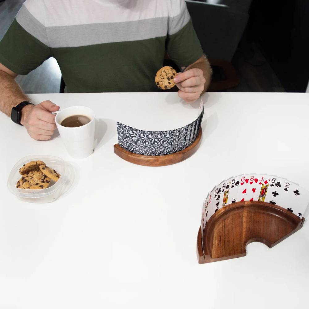 A person hodling coffee and cookie while playing cards with the card holder